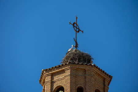 a large stork nest on the church tower against a blue sky with birds