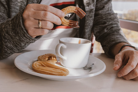 close-up of a man eating a typical sweet Spanish breakfast and churros with chocolateの写真素材