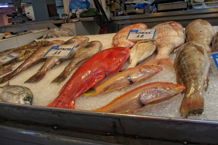 A display of various fresh fish is laid out on a bed of ice at a market, with price tags indicating their costの写真素材