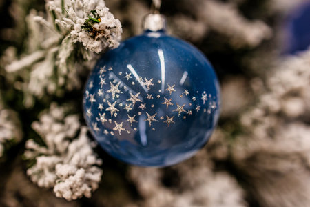 A blue ornament decorated with silver stars hangs delicately on a snowy Christmas tree branchの写真素材