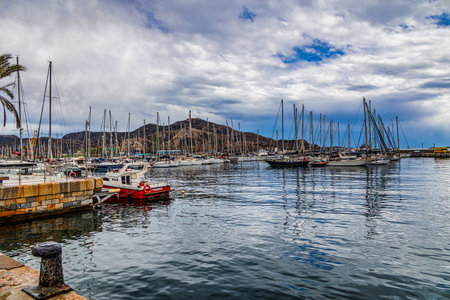 A bustling marina is filled with numerous sailboats, their masts reaching up towards a partly cloudy skyの写真素材