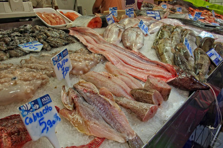 A display of various fresh fish is laid out on a bed of ice at a market, with price tags indicating their costの写真素材