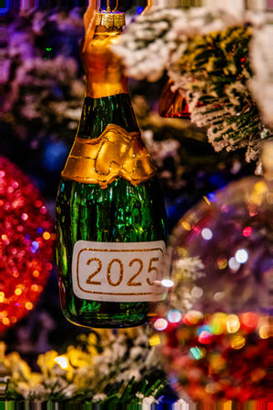 A festive ornament shaped like a champagne bottle hangs on a Christmas tree, adorned with a 2025 labelの写真素材