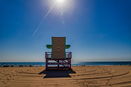 A bright sun shines over a lifeguard chair on an empty beachの写真素材