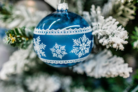 A blue ornament decorated with silver stars hangs delicately on a snowy Christmas tree branchの写真素材