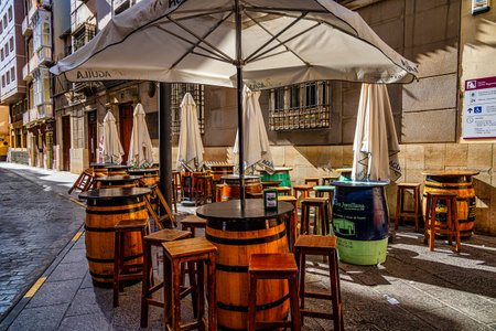 Outdoor cafÃ© tables and chairs are set up on a quaint cobblestone street, featuring barrels as table bases and shade umbrellas overhead.の写真素材