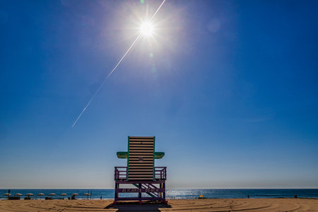 A bright sun shines over a lifeguard chair on an empty beachの写真素材
