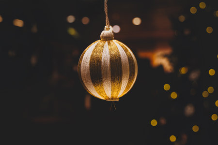 A glittering, gold ornament hangs against a backdrop of blurred, warm, twinkling lightsの写真素材