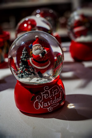 snow globe features a cheerful Santa Claus and a decorated Christmas tree, with Feliz Navidad written on its red baseの写真素材