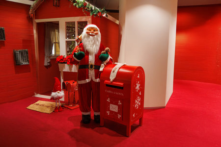Santa Claus stands next to a red mailbox designated for letters to him, surrounded by festive decorations.の写真素材