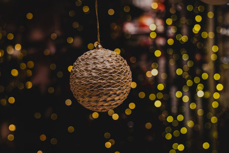 A glittering, gold ornament hangs against a backdrop of blurred, warm, twinkling lightsの写真素材