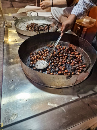 A person roasts chestnuts in a large metal pan using a spatula-like tool.の写真素材
