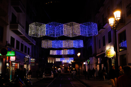 Colorful geometric lights hang above a lively urban street, illuminating the night scene Alicante spainの写真素材