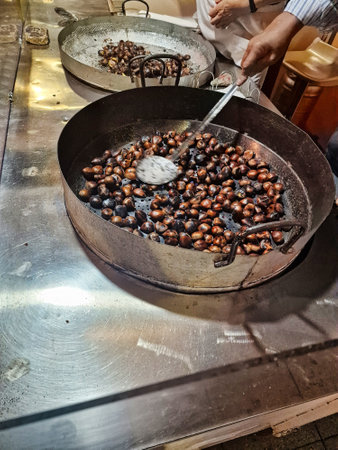 A person roasts chestnuts in a large metal pan using a spatula-like tool.の写真素材
