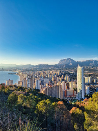 A coastal cityscape Benidorm is bathed in the warm glow of a setting sun, with high-rise buildings clustering along the shorelineの写真素材