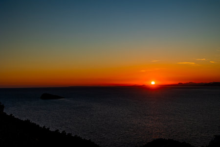 A serene sunset casts a warm orange glow over the horizonの写真素材