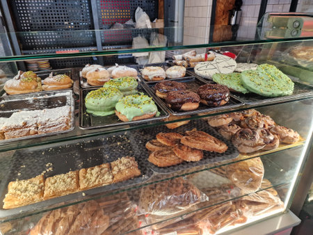 A variety of delicious pastries and baked goods are displayed on trays inside a glass counterの写真素材