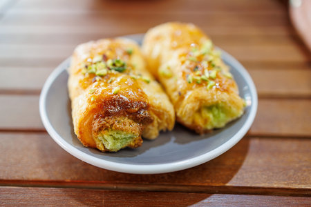 Two flaky pastries filled with green cream sit on a gray plate, their tops garnished with chopped nutsの写真素材
