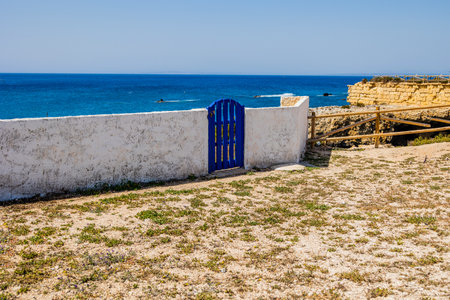 A white wall with a vibrant blue gate overlooks a serene coastal landscape. In the backgroundの写真素材