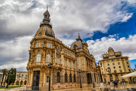An ornate historic building stands majestically under a partly cloudy sky, featuring intricately architectural details and a prominent clock towerの写真素材