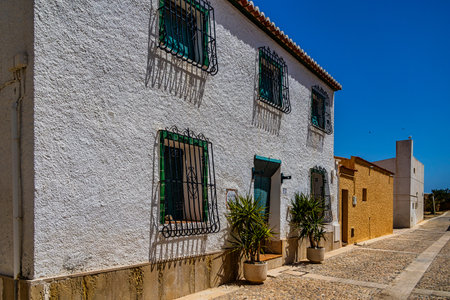 A narrow cobblestone street lined with colorful houses basks under a clear blue sky.の写真素材