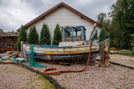 A weathered fishing boat rests on a gravel area in front of a houseの写真素材