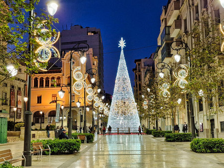 A brightly lit Christmas tree stands at the center of a bustling city street, surrounded by elegant buildings.の写真素材