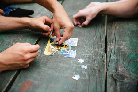 Teenagers collect puzzles on a wooden green table in the open airの写真素材