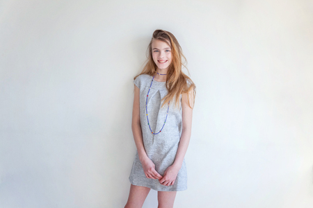 Happy teenage girl smiling. Closeup portrait young happy positive woman in grey dress at home in bright room against white wall. European woman. Positive human emotion facial expression body languageの写真素材