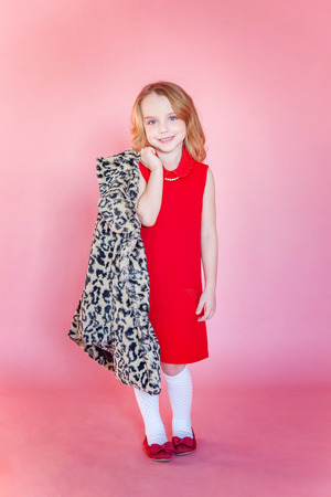 Little cute sweet smiling girl in red dress standing on pink colourful pastel trendy modern fashion pin-up backgroundの写真素材