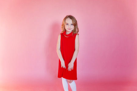 Little cute sweet smiling girl in red dress standing on pink colourful pastel trendy modern fashion pin-up backgroundの写真素材