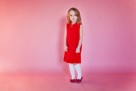 Little cute sweet smiling girl in red dress standing on pink colourful pastel trendy modern fashion pin-up backgroundの写真素材