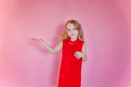 Little cute sweet smiling girl in red dress standing on pink colourful pastel trendy modern fashion pin-up backgroundの写真素材