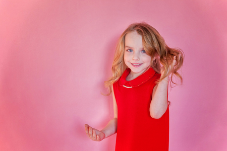 Little cute sweet smiling girl in red dress standing on pink colourful pastel trendy modern fashion pin-up backgroundの写真素材
