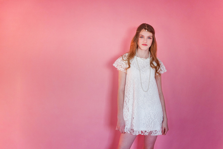 Happy teenage girl smiling. Closeup portrait young happy positive woman wearing white dress standing on pink colourful pastel trendy modern fashion pin-up background. European woman. Positive human emotion facial expression body languageの写真素材