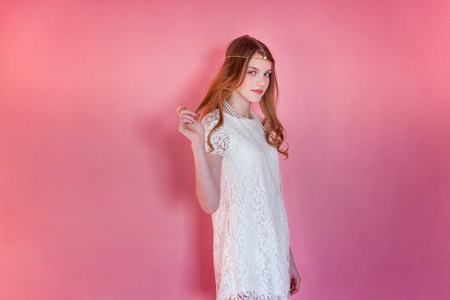Happy teenage girl smiling. Closeup portrait young happy positive woman wearing white dress standing on pink colourful pastel trendy modern fashion pin-up background. European woman. Positive human emotion facial expression body languageの写真素材