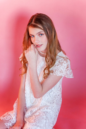 Happy teenage girl smiling. Closeup portrait young happy positive woman wearing white dress standing on pink colourful pastel trendy modern fashion pin-up background. European woman. Positive human emotion facial expression body languageの写真素材