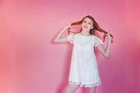 Happy teenage girl smiling. Closeup portrait young happy positive woman wearing white dress standing on pink colourful pastel trendy modern fashion pin-up background. European woman. Positive human emotion facial expression body languageの写真素材