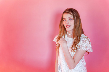 Happy teenage girl smiling. Closeup portrait young happy positive woman wearing white dress standing on pink colourful pastel trendy modern fashion pin-up background. European woman. Positive human emotion facial expression body languageの写真素材