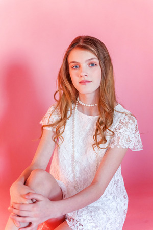Happy teenage girl smiling. Closeup portrait young happy positive woman wearing white dress standing on pink colourful pastel trendy modern fashion pin-up background. European woman. Positive human emotion facial expression body languageの写真素材