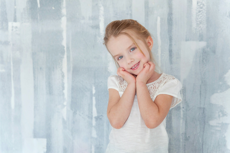 Sweet happy little girl in blank white t-shirt standing against grey textured wall backgroundの写真素材