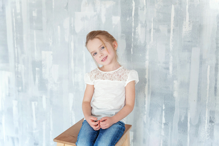 Sweet happy little girl in blank white t-shirt sitting on chair against grey textured wall backgroundの写真素材
