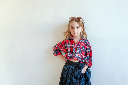 Sweet happy adorable fashion young little girl dressed like hipster hippie gipsy cowboy in sunglasses standing against white wall background in light bright room. Lifestyle people trendy conceptの写真素材