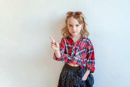 Sweet happy adorable fashion young little girl dressed like hipster hippie gipsy cowboy in sunglasses standing against white wall background in light bright room. Lifestyle people trendy conceptの写真素材