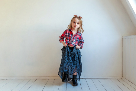 Sweet happy adorable fashion young little girl dressed like hipster hippie gipsy cowboy in sunglasses standing against white wall background in light bright room. Lifestyle people trendy conceptの写真素材
