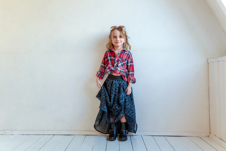 Sweet happy adorable fashion young little girl dressed like hipster hippie gipsy cowboy in sunglasses standing against white wall background in light bright room. Lifestyle people trendy conceptの写真素材