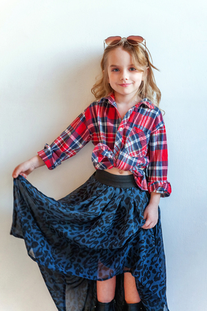 Sweet happy adorable fashion young little girl dressed like hipster hippie gipsy cowboy in sunglasses standing against white wall background in light bright room. Lifestyle people trendy conceptの写真素材