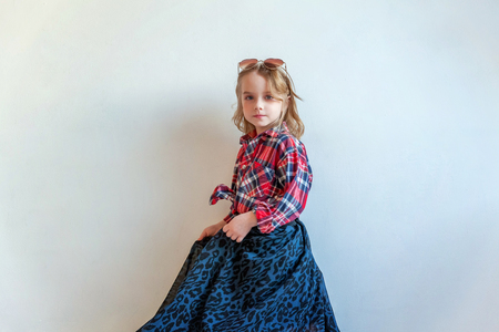 Sweet happy adorable fashion young little girl dressed like hipster hippie gipsy cowboy in sunglasses standing against white wall background in light bright room. Lifestyle people trendy conceptの写真素材