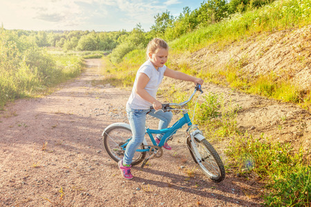 Happy child riding bike. Young girl on bicycle in sunny summer park. Healthy school children summer activity. Kids playing and cycling outdoors. Little girl learns to keep balance while riding bicycleの写真素材