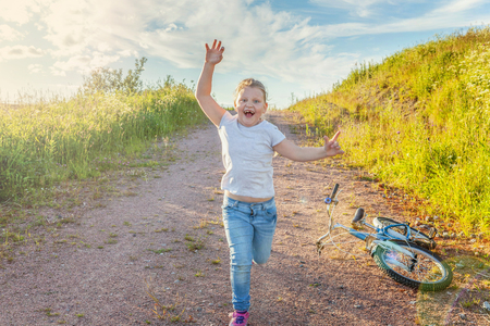 Happy cute little girl running on the road in the park. Happiness. Young little girl with bicycle in sunny summer park. Healthy school children summer activity. Kids playing and cycling outdoorsの写真素材